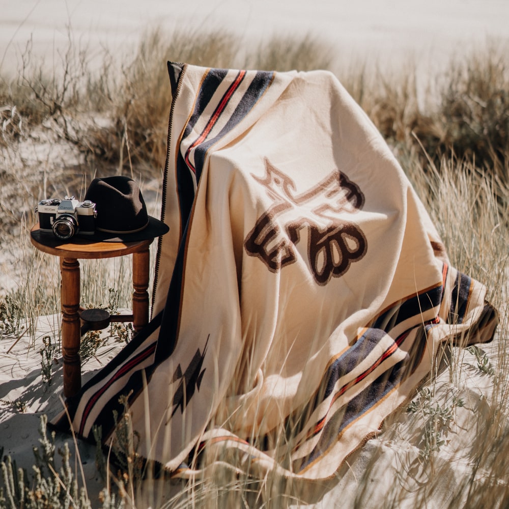 An Anifurry thunderbird merino wool blanket draped over a wooden chair in a grassy field, with a camera placed on the desk.