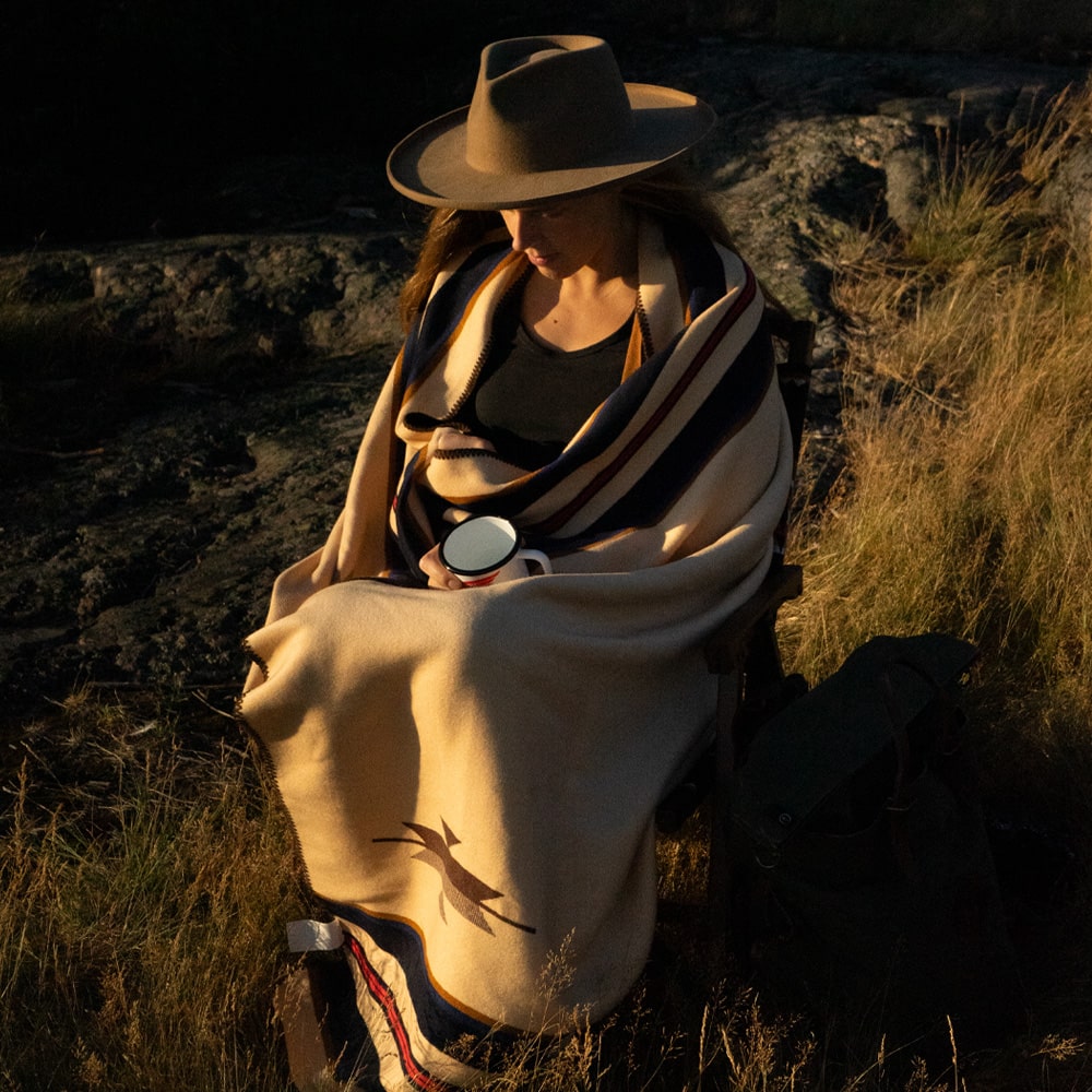 A woman wearing an Anifurry Thunderbird Merino Wool Blanket sat in a chair.